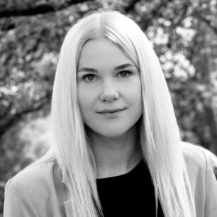 Kvinna med långt, rakt hår tittar in i kameran, med en suddig bakgrund av träd.