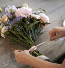 Händer binder ett band runt en bukett med blommor på ett bord.