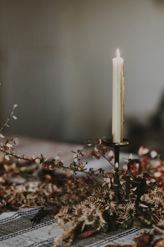 Ett brinnande ljus på en ljusstake omgiven av torkade blommor.