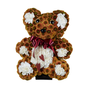 Nallebjörn gjord av blommor, dekorerad med vita blommor och en röd rosett runt halsen, samt två hängande hjärtan.